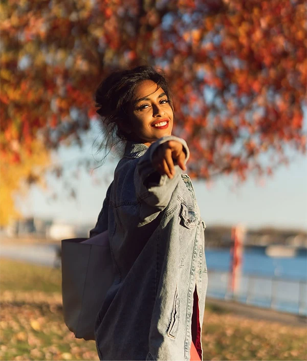 Woman smiling under orange autumn leaves by the lake